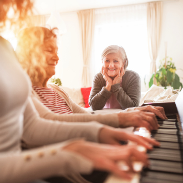 Older woman watching two people play the piano together.