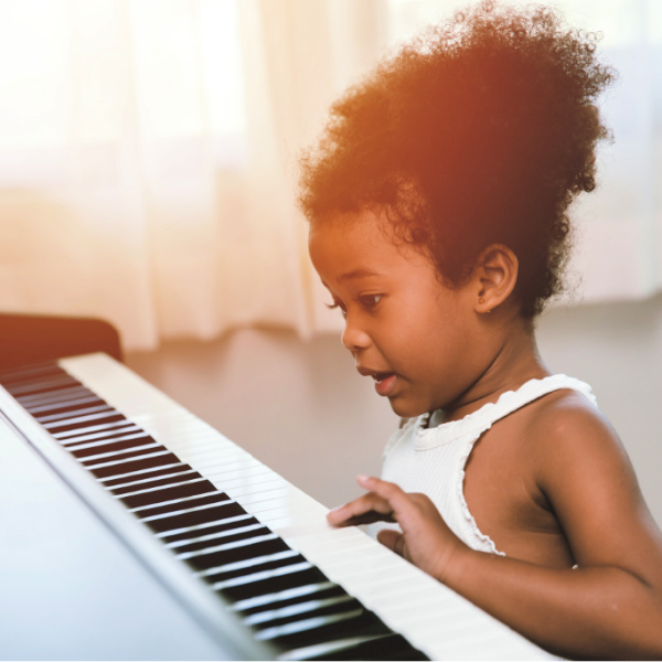 Young Black girl gently pressing the keys of a piano.