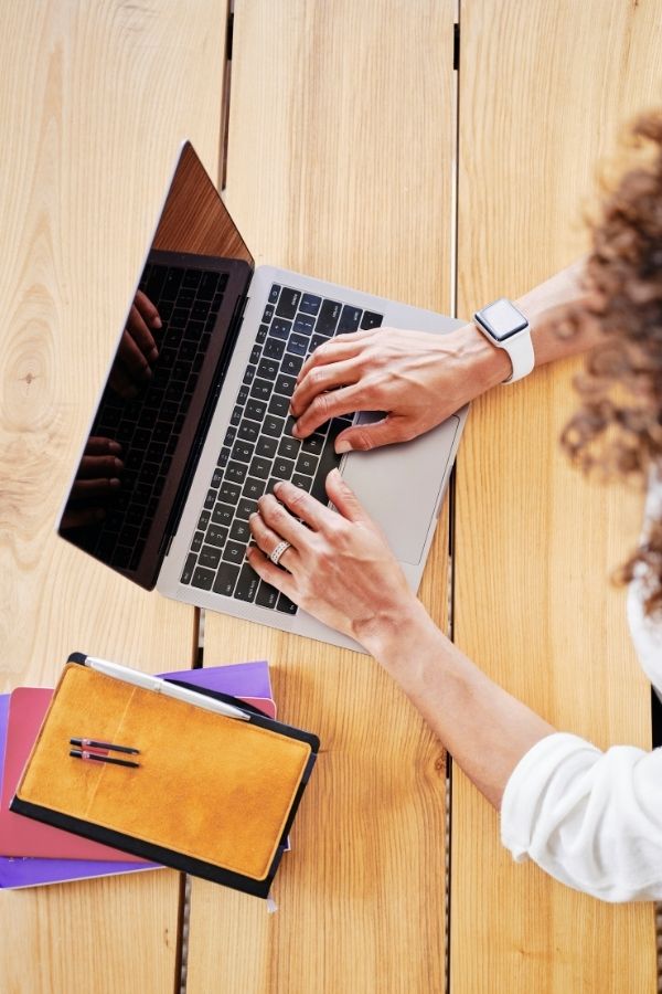 Overhead picture of a woman typing on a laptop computer with several notebooks next to her.